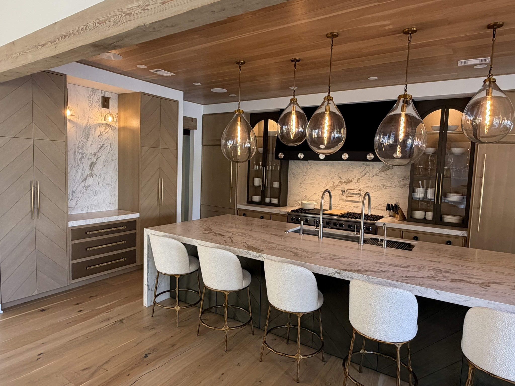 Custom kitchen with wood ceiling, pendant lights, and marble island