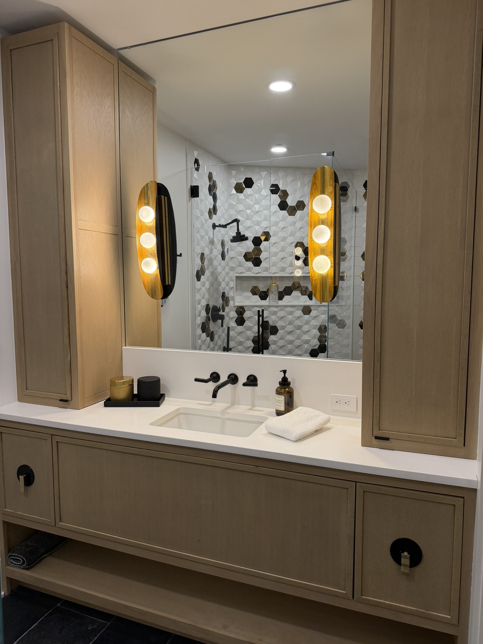 Oak vanity with tower cabinets and hex tile mirror reflection