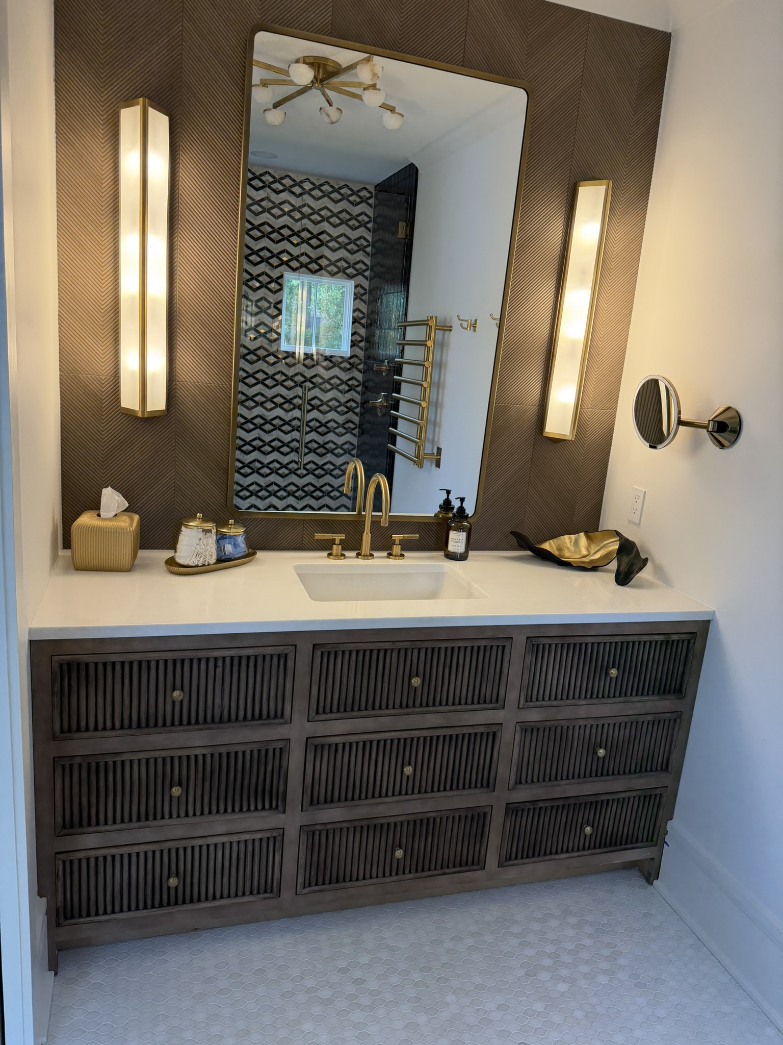 Dark fluted vanity with chevron wood wall and brass fixtures