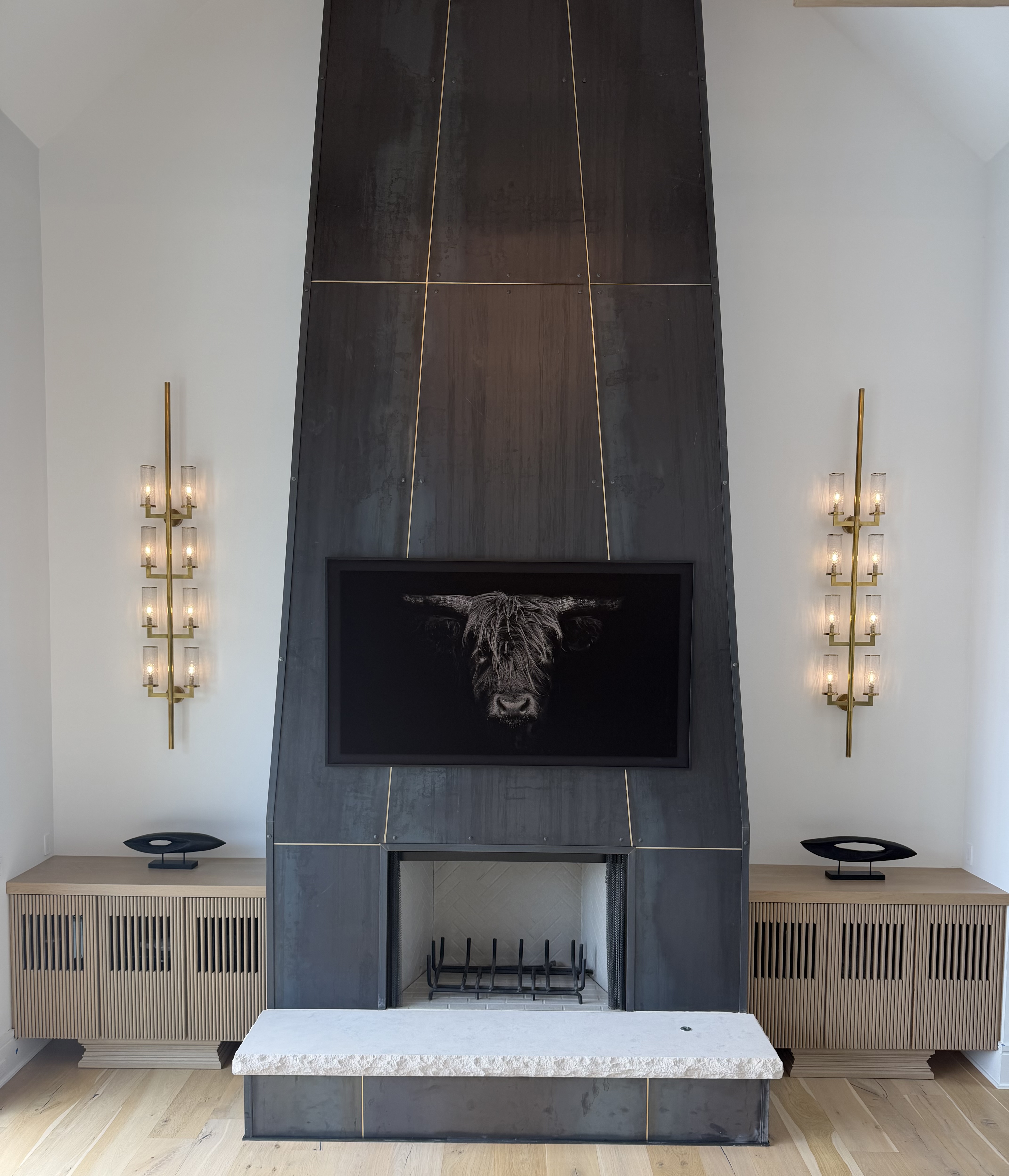 Dramatic fireplace surround with flanking slatted oak cabinets and brass sconces
